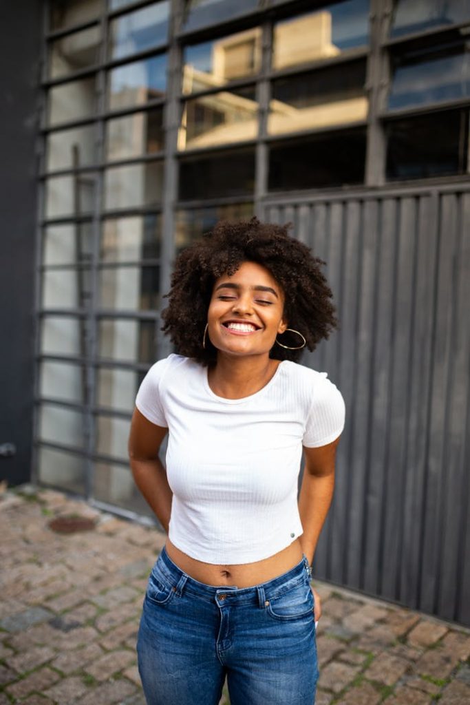 pexels photo 2701660 Smiling woman with curly hair in casual fashion enjoys a bright day outdoors.