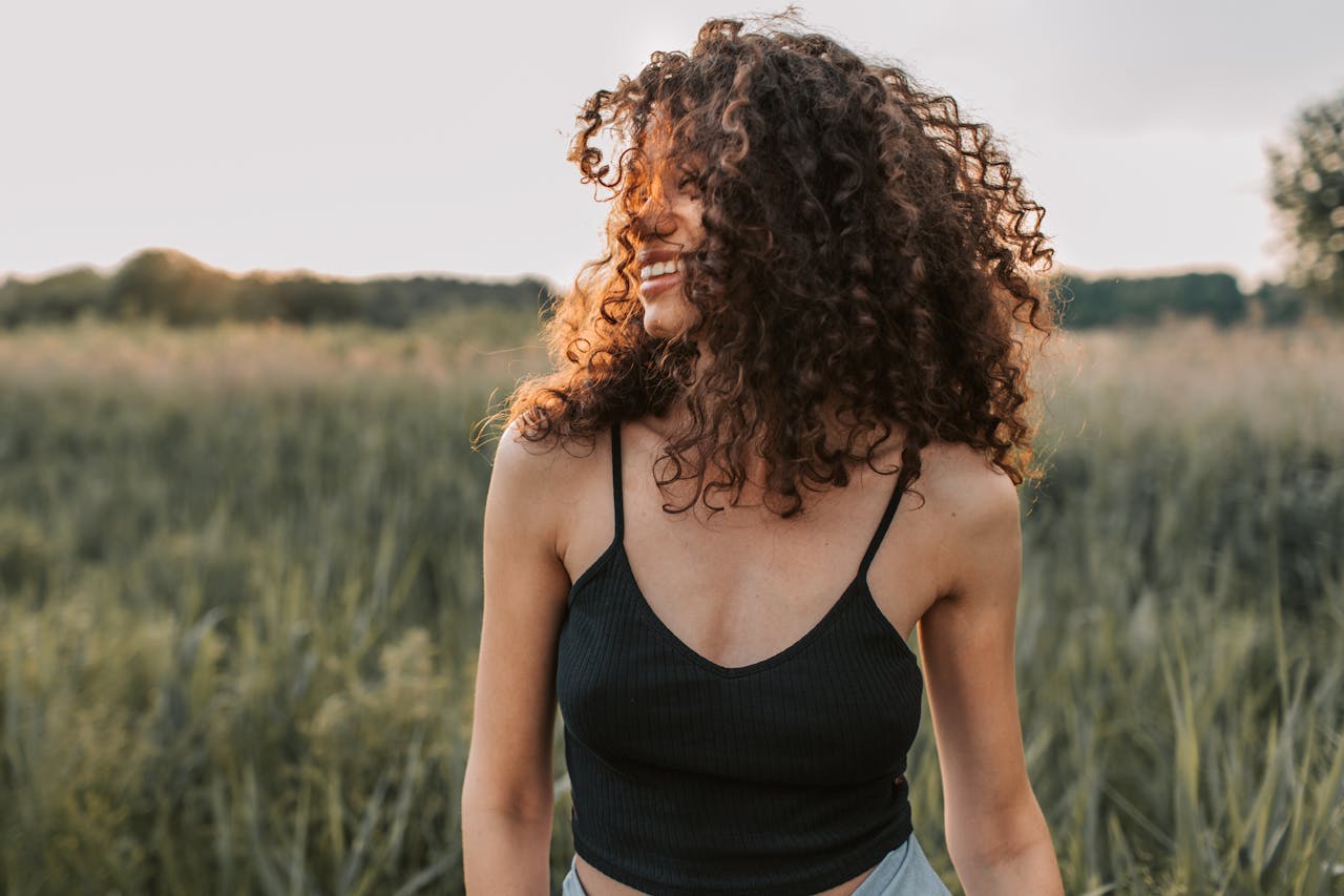 A cheerful woman in casual attire enjoying a sunny day outdoors with natural curly hair.